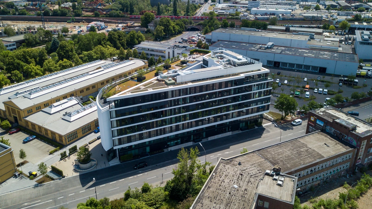 Unser eigens errichtetes Office konnten wir nach unseren Vorstellungen gestalten: Nachhaltig, digital und zukunftsorientiert.   Gebaut wurde das Ship im Einklang mit unseren Werten nach Gold Standard der deutschen Gesellschaft für Nachhaltiges Bauen e.V.  Angelehnt an den New Work - Gedanken verfügt das Gebäude über eine Infrastruktur und Ausstattung, die sich komplett nach unseren Bedürfnissen orientiert und entscheidend zum persönlichen Wohlbefinden beiträgt.   Für jede Arbeitssituation gibt es passende Angebote: Meetingräume, Creative Labs, Think Tanks, Phone Capsules, Lounges, Gärten oder Coffee Corner. Unterstützt wird das Konzept durch digitales Raummanagement.   Mit unserer Ship App buchen wir Meetingräume, öffnen Türen, senken die Raumtemperatur und checken den Speiseplan.